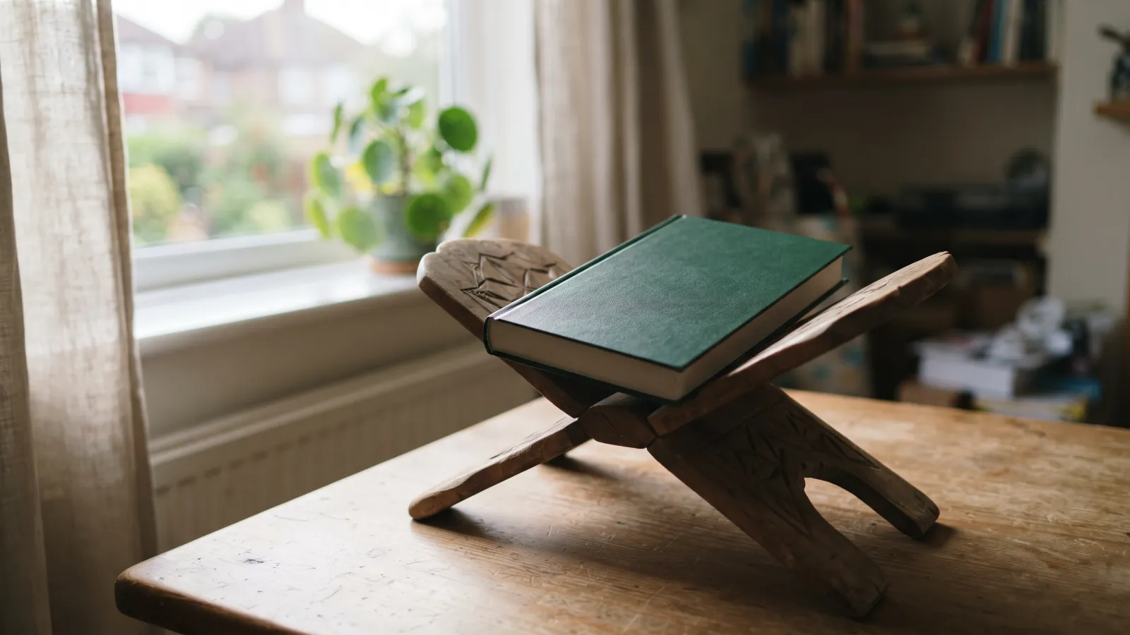 A closed Quran on a wooden rehal stand beside a sunny window at home